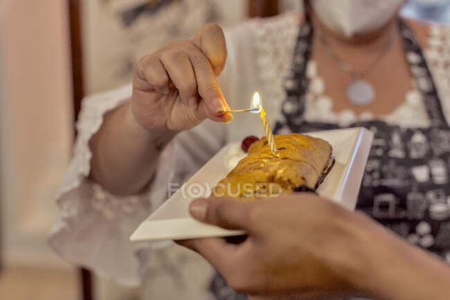 Crop anonymous cafeteria employees lighting birthday candle on tasty berry pastry on plate at work — Stock Photo