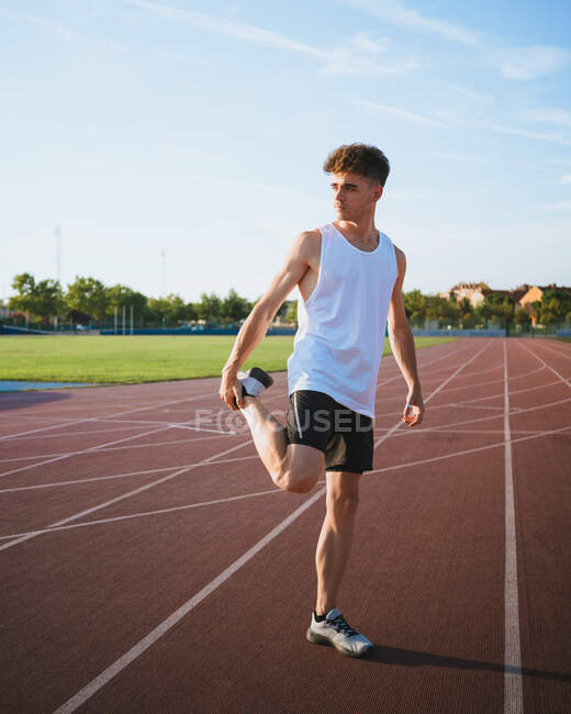 Jovem atleta do sexo masculino em desgaste ativo olhando para longe durante o treinamento na pista sob céu nublado na cidade — Fotografia de Stock