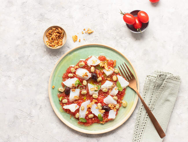 Sommerlicher Tomaten-Kabeljau-Salat in einer flachen Schüssel mit Gabel und einer Schüssel gebratener Zwiebeln — Stockfoto