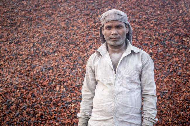 ÍNDIA, BANGLADESH - DEZEMBRO 7, 2015: Macho indiano étnico em roupas sujas olhando para a câmera com pilha de pedras no fundo do forno de tijolos na Índia — Fotografia de Stock
