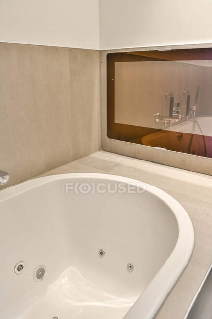 Деталь белого керамическая ванна расположена в современной ванной комнате с бежевой плиткой стены — стоковое фото