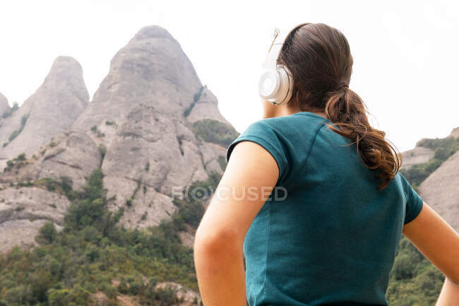 Fro below dreamy female tourist enjoying song from wireless headset against Montserrat and trees in Spain — Stock Photo
