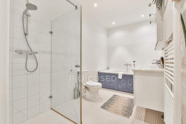 Санузел и ванна в просторной ванной комнате с керамической раковиной и туалетом и выложенными плиткой стенами — стоковое фото