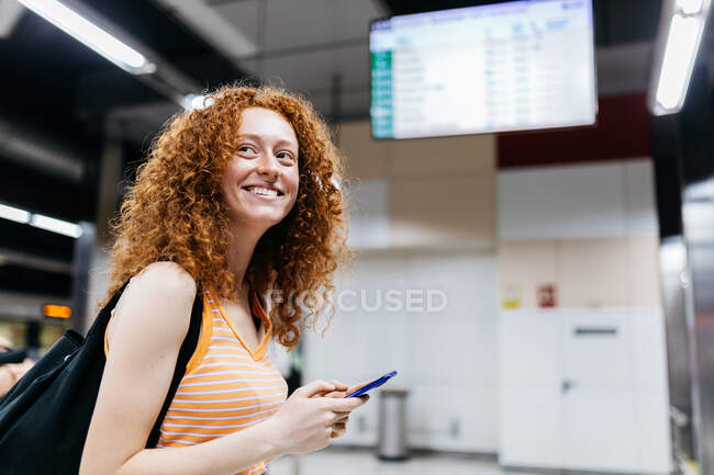 Vue latérale de la femme avec téléphone portable et sac à dos regardant loin sur la plate-forme de métro — Photo de stock