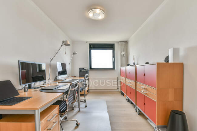 Desktop computers and laptop against armchairs and cabinets on parquet under lamp in contemporary workspace — Stock Photo