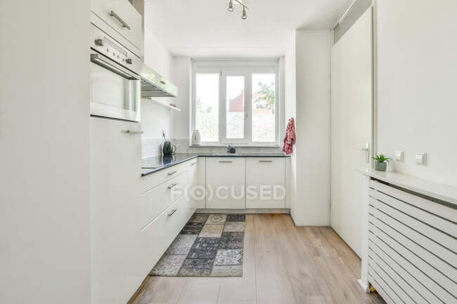 Interior of stylish kitchen with white cabinets and colorful carpet on parquet in apartment in daytime — Stock Photo