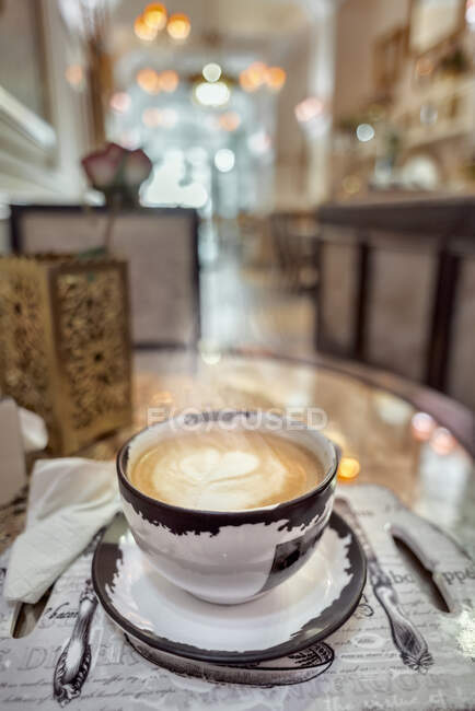 Ceramic cup of aromatic coffee with latte art on table with napkins and blooming rose in cafeteria — Stock Photo