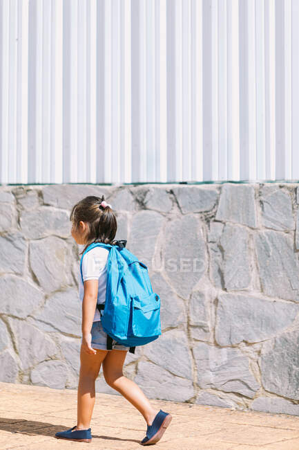 Вид сбоку школьника с рюкзаком на тротуаре, смотрящего вперед при солнечном свете — стоковое фото