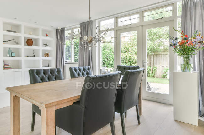 Wooden table and black leather chairs placed in spacious light dining room in modern house in daytime — Stock Photo