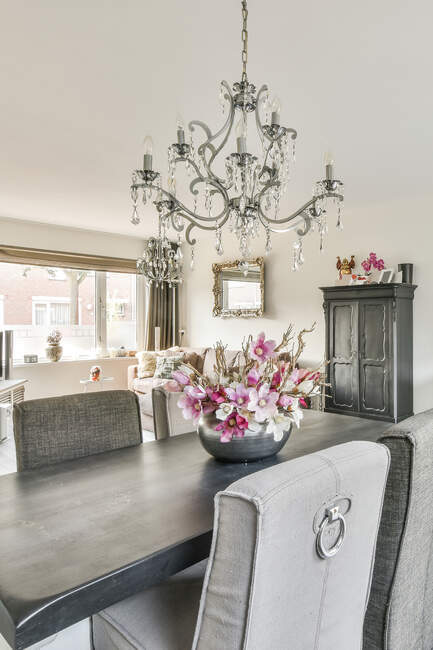 Mazzo di fiori rosa disposti su tavolo in legno in sala da pranzo con lampadario classico in appartamento di lusso — Foto stock