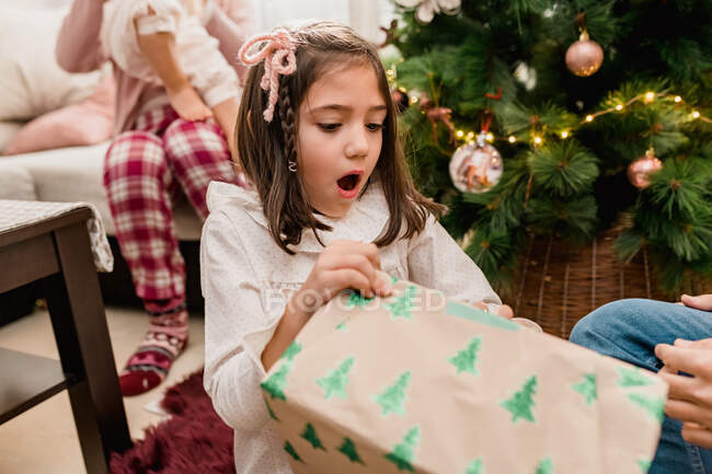Удивленный ребенок открывает подарок коробку между родителями урожая и братом и сестрой во время празднования новогоднего праздника в доме — стоковое фото