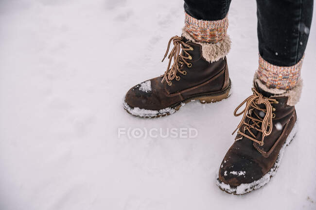De dessus de la culture personne méconnaissable dans des chaussettes colorées chaudes et des bottes debout sur un sol enneigé en hiver en plein jour — Photo de stock