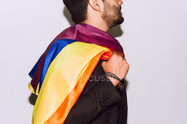 Crop unrecognizable bearded male playing and waving multicolored flag symbol of LGBTQ pride — Stock Photo