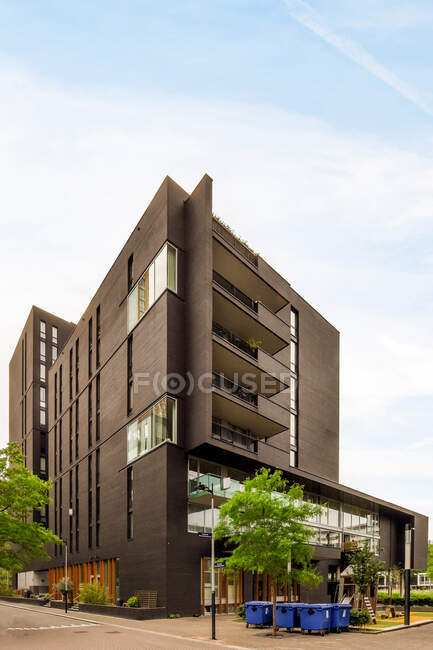 Contemporary multistory house exterior with balconies against trees and trash containers on pavement under cloudy sky in Amsterdam — Stock Photo