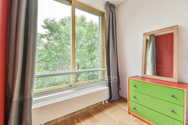 Quarto contemporâneo interior com cômoda e espelho contra janela com cortinas em casa de luz — Fotografia de Stock