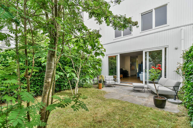 Wohnhausaußenseite mit Glaswand gegen Hinterhof mit Couch und grünem Baum auf Wiese im Sommer — Stockfoto