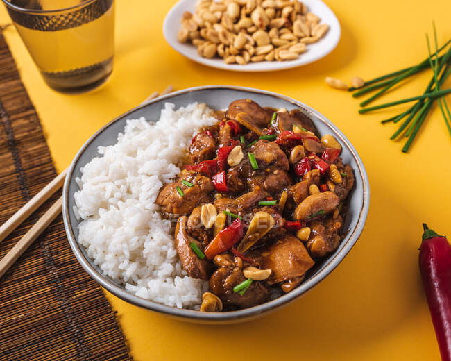 De cima tigela de composição com frango kung pao com arroz branco amendoim e pimenta vermelha quente e cebola verde e pauzinhos — Fotografia de Stock