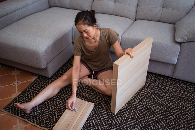 Barefoot ethnic female mounting table while sitting with crossed legs on ornamental carpet against sofa in house — Stock Photo
