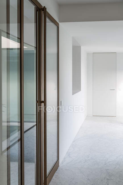 Интерьер просторного коридора с белыми стенами и стеклянными дверями в современной квартире — стоковое фото