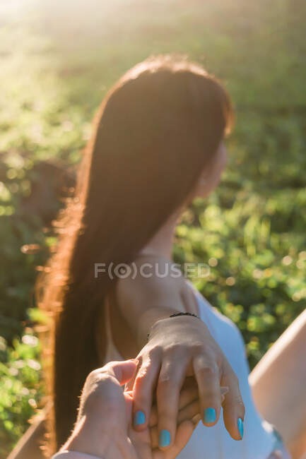 Side view of unrecognizable female adolescent with long hair holding crop best friend by hand in back lit — Stock Photo