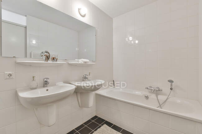 Интерьер пустой светлой ванной комнаты с ванной и раковинами под зеркалом — стоковое фото
