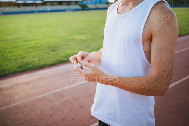 Crop young male athlete in undershirt putting on earbud while looking away in stadium — Stock Photo