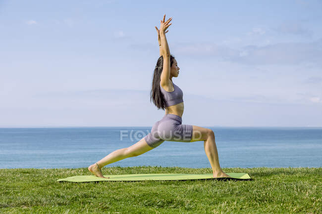 Vista lateral da jovem fêmea étnica em sportswear em pé em Ashta Chandrasana pose durante a prática de ioga na costa do mar — Fotografia de Stock