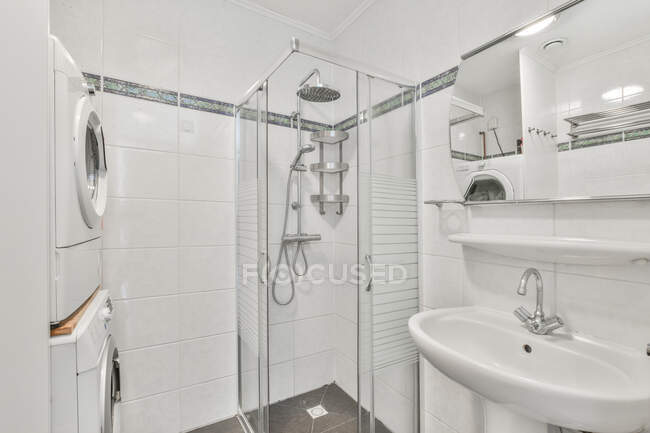 Cabine de chuveiro e máquinas de lavar roupa em banheiro moderno com paredes de azulejos brancos e pia de cerâmica — Fotografia de Stock