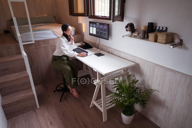 High angle full body of concentrated Asian female working on computer with charts showing dynamic of changes in value of cryptocurrency at convenient workplace — Stock Photo