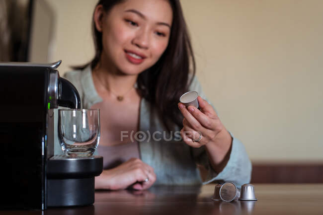 Crop smiling young ethnic female putting coffee pod in maker on table in house kitchen — Stock Photo