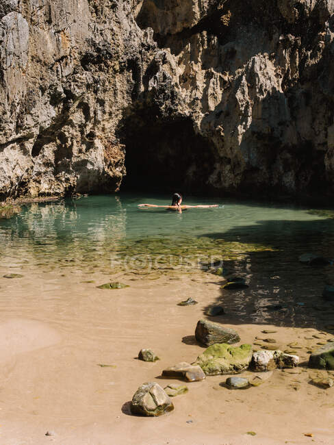 Faceless female traveler swimming in clear transparent seawater surrounded by rocky rough cave during summer holidays — Stock Photo