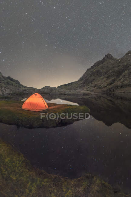 Vista panoramica della tenda sulla riva del lago contro la montagna innevata sotto cielo nuvoloso in serata — Foto stock