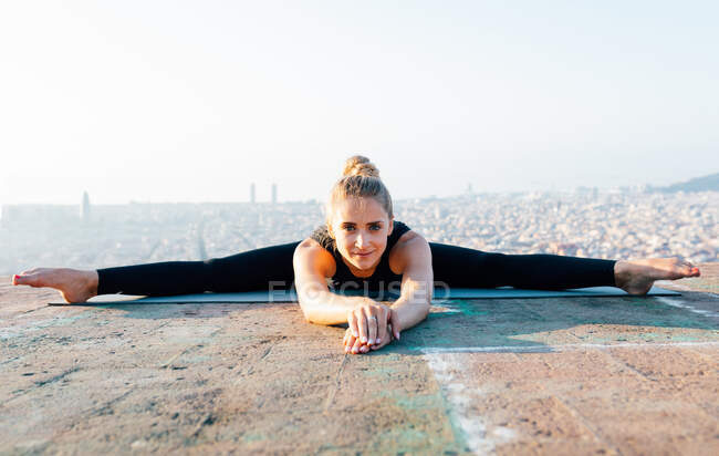 Все тело сконцентрированной молодой женщины практикующей Упавишта Конасана во время занятий йогой на открытом воздухе на крыше на закате — стоковое фото