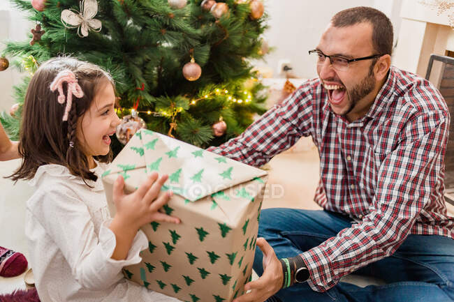 Smiling child opening present box between cheerful father during New Year holiday at home — Stock Photo
