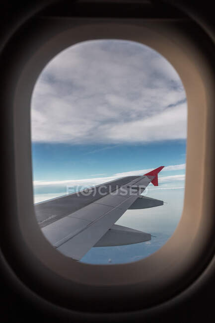 Through aircraft window view of fluffy clouds above sea and terrain during trip in daytime — Stock Photo
