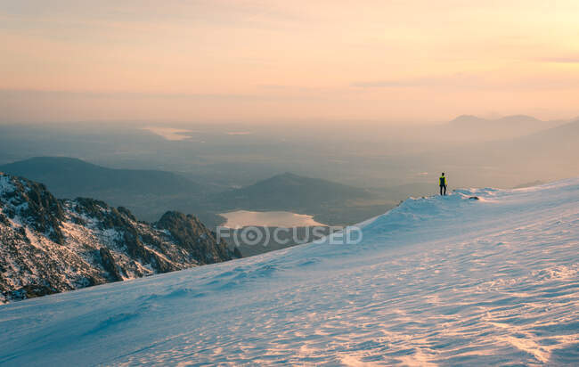 Viajero de pie en la cima de la montaña nevada y admirando el espectacular paisaje de las tierras altas en la Sierra de Guadarrama en España a la luz del sol - foto de stock