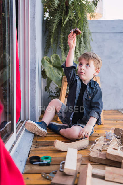 Criança encantadora brincando com automóveis de brinquedo entre peças de madeira e banquinho artesanal à luz do dia — Fotografia de Stock