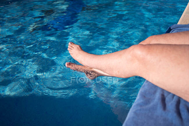 De cima de colheita anônimo descalço viajante feminino sentado na borda da piscina com pernas cruzadas em água azul pura — Fotografia de Stock