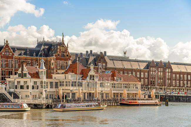 Edifici storici in mattoni situati sulla riva del fiume con barche ormeggiate nel centro storico di Amsterdam — Foto stock