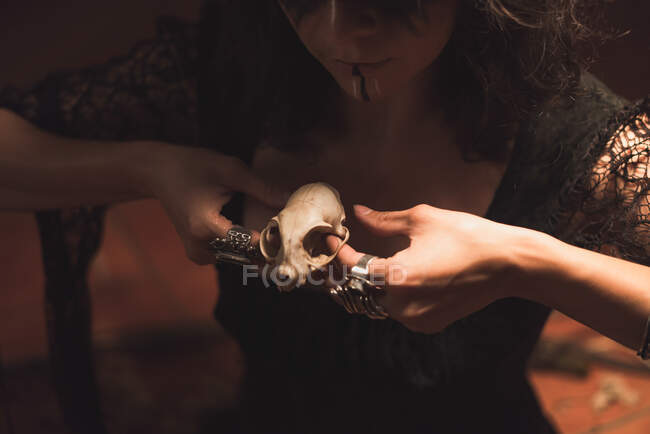Cropped unrecognizable enchantress with painted face and skull casting spell during mystic ritual in room with dim light — Stock Photo