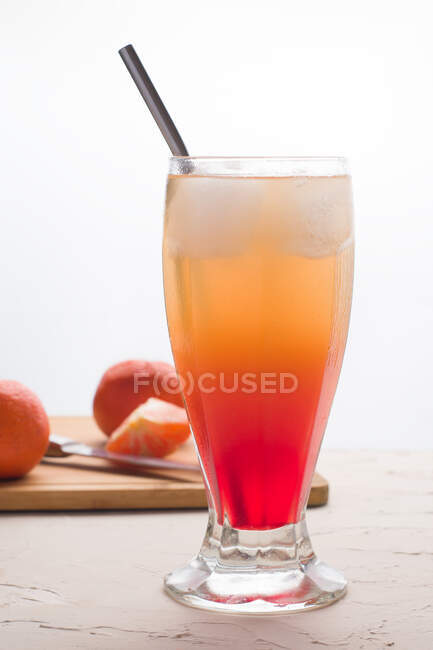 Copo de refrescante cocktail Sunrise com cubos de gelo e palha servida na mesa com laranjas frescas — Fotografia de Stock