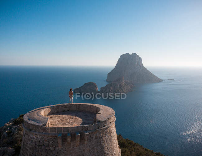 Vista aérea traseira do turista masculino anônimo admirando formações rochosas e mar ondulado da torre velha em Ibiza Espanha — Fotografia de Stock