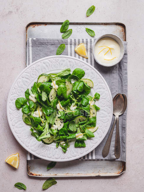 Draufsicht auf köstlichen grünen Salat mit frischen Gurkenstücken und Spinatblättern mit schwarzem Sesam gegen Zitronensauce — Stockfoto
