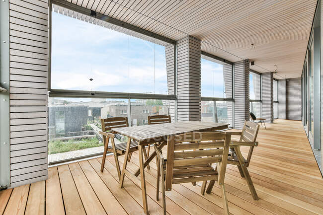 Інтер'єр балкона з дерев'яним столом і кріслами проти вікон і колон під стелею в домашніх умовах — стокове фото