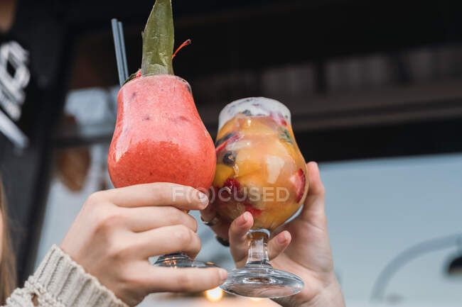 Crop unrecognizable best female friends clinking glasses of tasty refreshing drinks with fruit pieces in urban cafeteria — Stock Photo