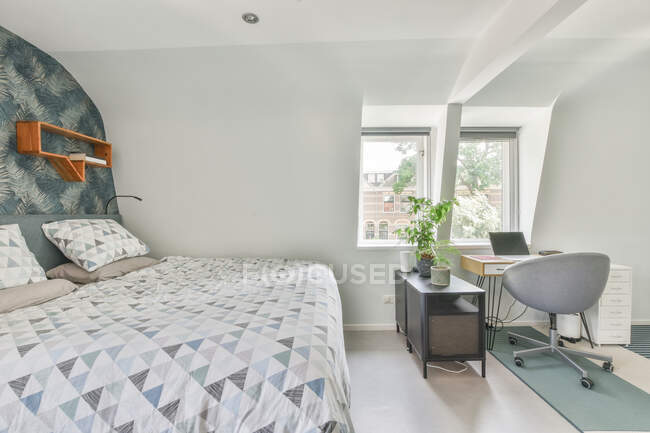 Weiches Bett mit weißer Bettwäsche in der Nähe des Arbeitsplatzes mit geöffnetem Laptop in geräumigem hellen Schlafzimmer in der Wohnung — Stockfoto