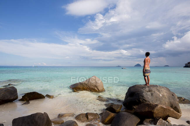 Back view full body of barefoot female tourist in swimwear standing on boulder and admiring azure sea during vacation in Malaysia — Stock Photo