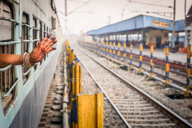 Nepal - November 29: Crop anonymous ethnic female with traditional mehndi ornament on hand waving out from train window — Stock Photo