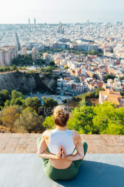 Desde arriba vista trasera de una mujer anónima flexible con las manos orantes detrás de la espalda practicando yoga en la alfombra en la ciudad soleada - foto de stock