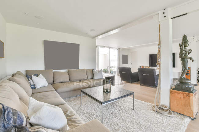 Interior moderno sala de estar com estátua no pedestal contra sofá e poltronas em tapete macio em casa de luz — Fotografia de Stock